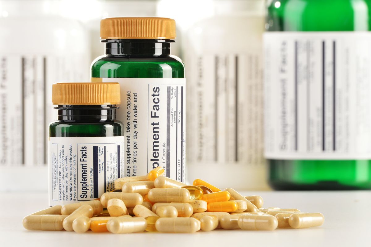 Two green supplement bottles with orange caps surrounded by various capsules and pills on a white background.