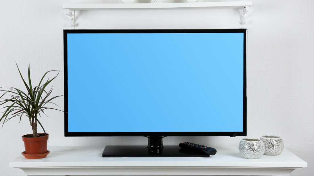 Flat-screen television with a blue display, set on a white table next to decorative items and a plant, showcasing a minimalist home entertainment setup.