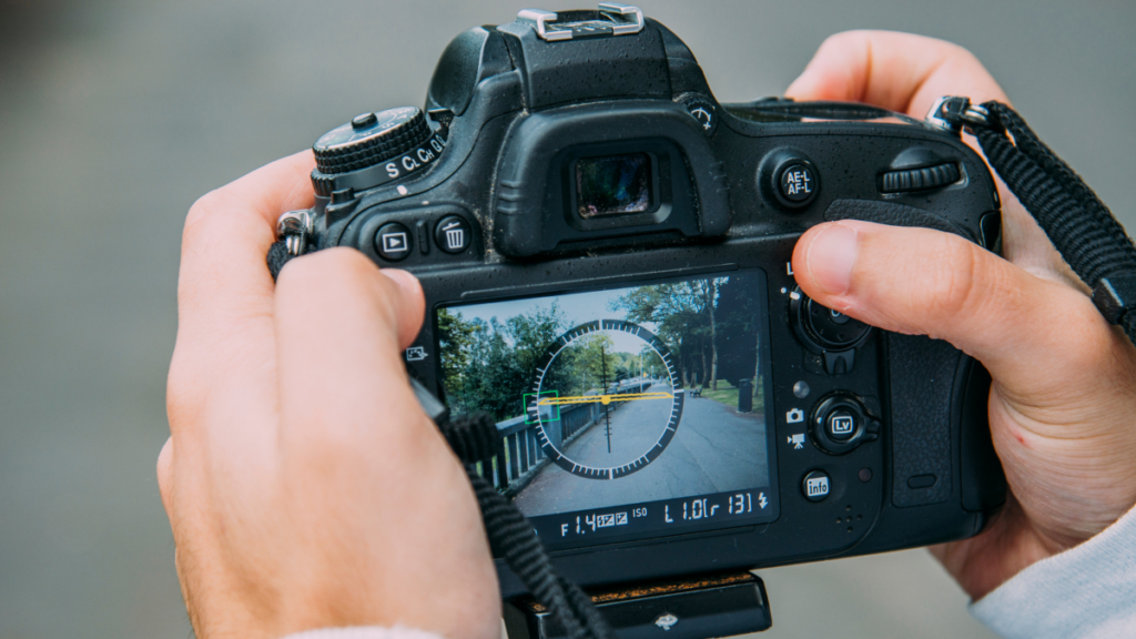 Photographer adjusting settings on a DSLR camera, capturing an outdoor scene through the viewfinder, with hands framing the device.