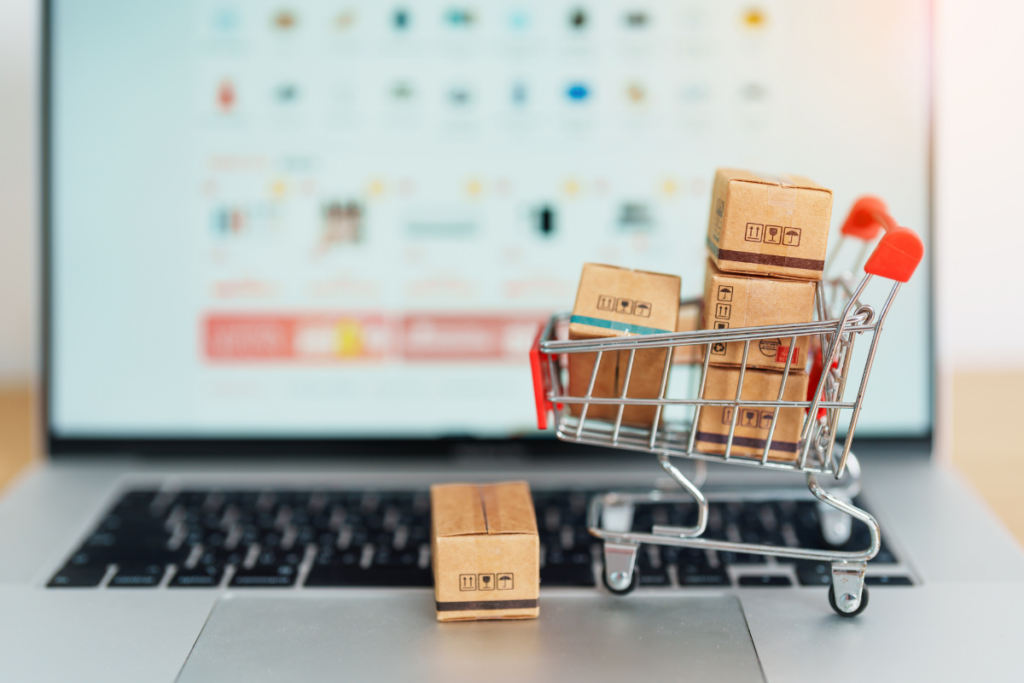 A miniature shopping cart filled with small cardboard boxes placed on a laptop keyboard, symbolizing online shopping and e-commerce.