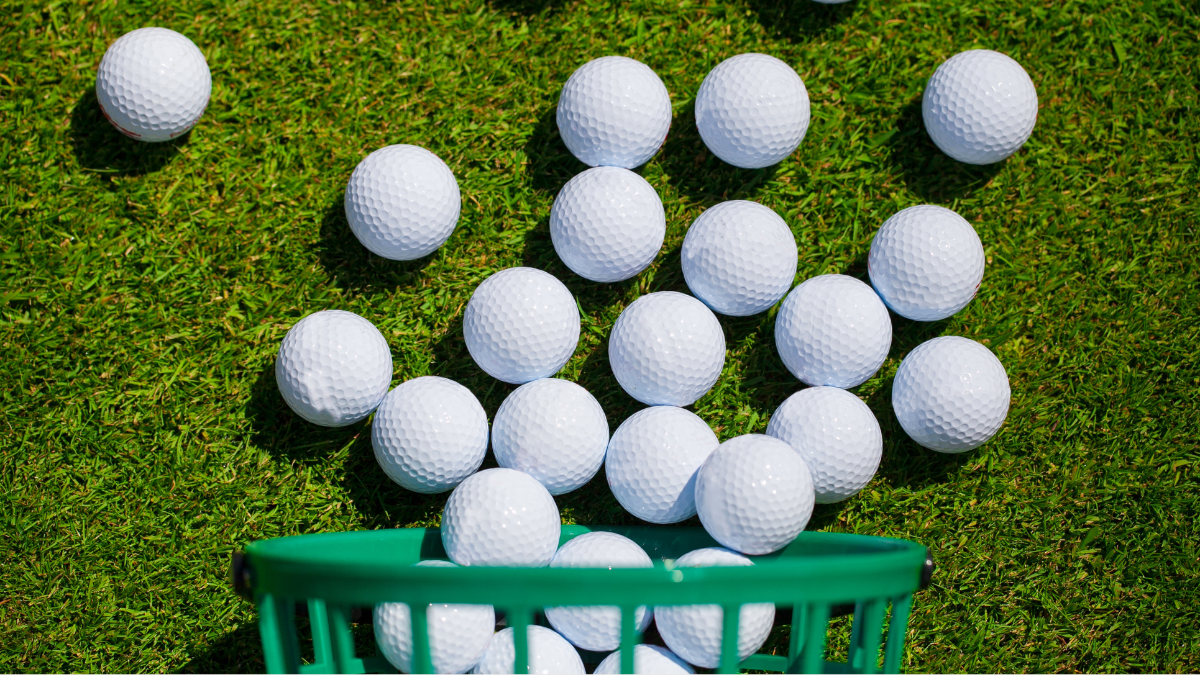 A vibrant scene of white golf balls spilling from a green basket onto a sunlit grassy surface, ready for practice.