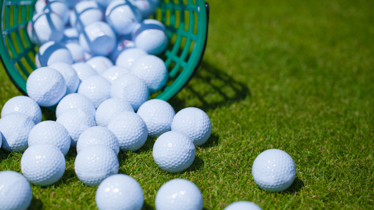 A basket of white golf balls tipped over on a lush green field, showcasing a perfect practice setup under bright daylight.