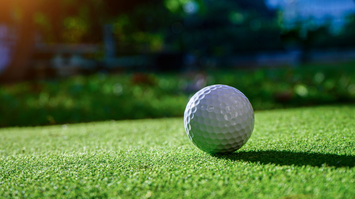A close-up of a golf ball resting on vibrant green grass under warm sunlight, capturing the essence of a peaceful day on the course.