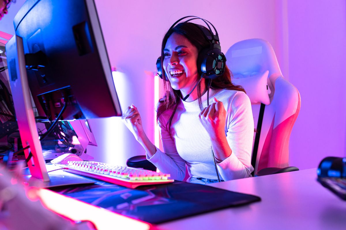 A gamer wearing headphones sits at a dual-monitor setup with colorful LED lighting, fully immersed in a futuristic game environment.