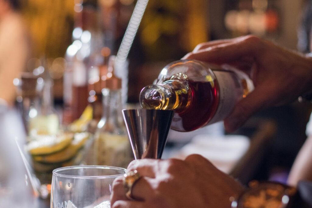 Hand pouring liquor into a jigger at a bar.