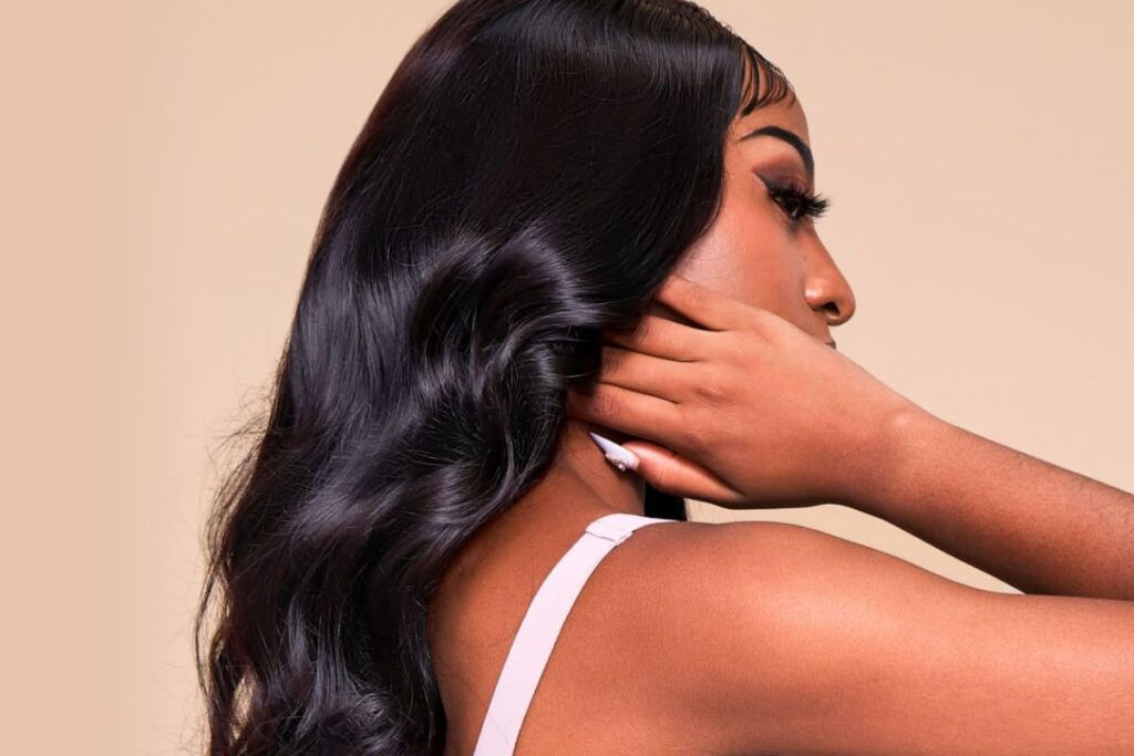 Side profile of a woman with long, wavy black hair, touching her hair with her hand.