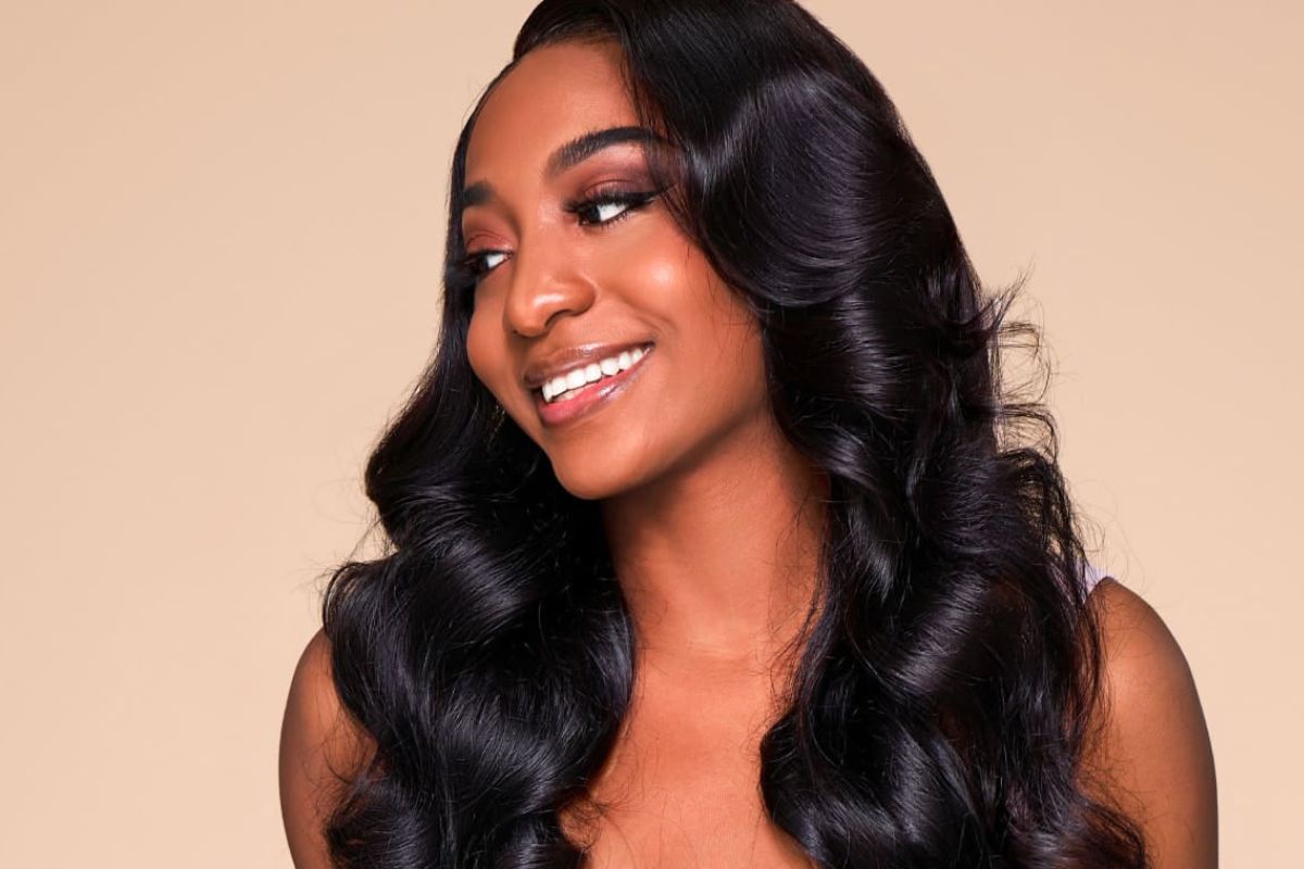 Woman smiling with long, wavy, shiny black hair against a neutral background.