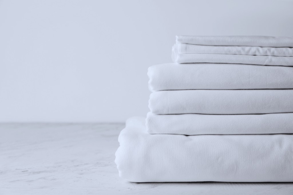 Minimalist stack of white folded linens placed on a clean, light surface with a plain background.