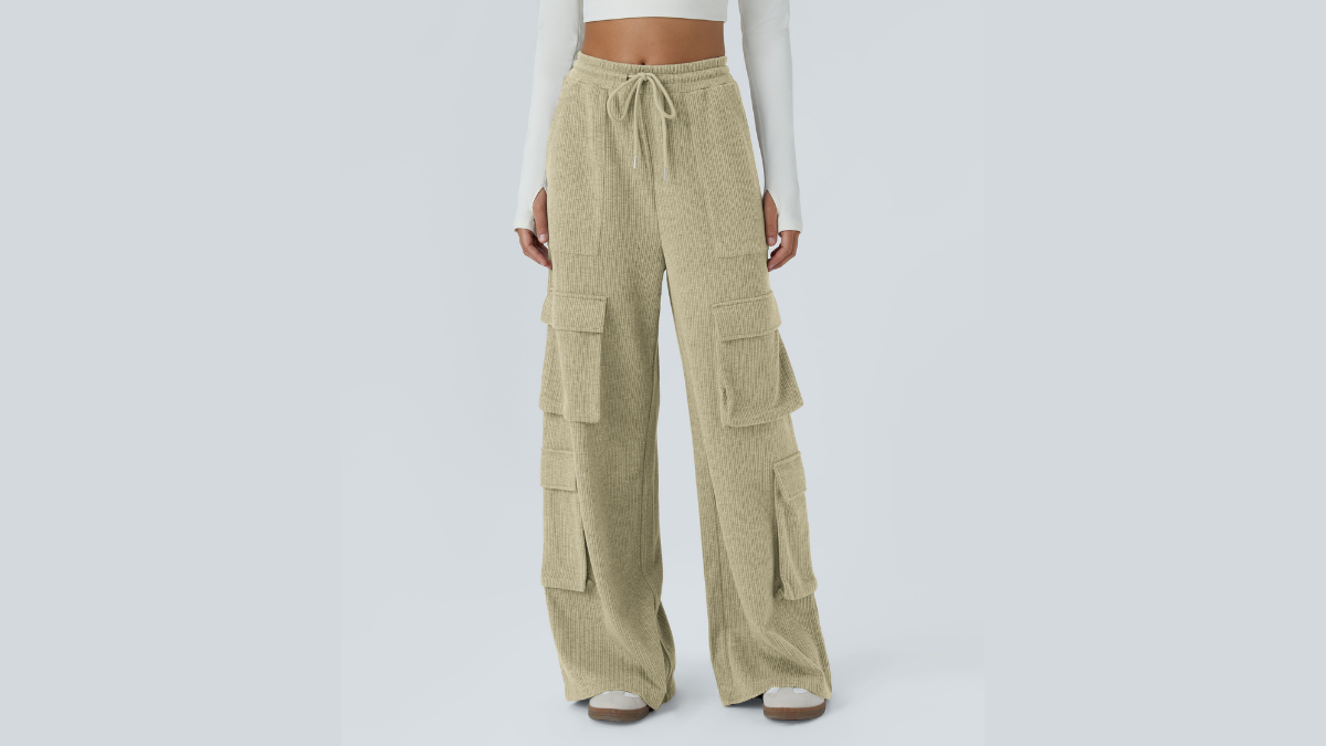 A model wearing beige corduroy cargo pants with multiple pockets, a drawstring waist, and wide legs, paired with a long-sleeve white crop top, standing against a light gray background.