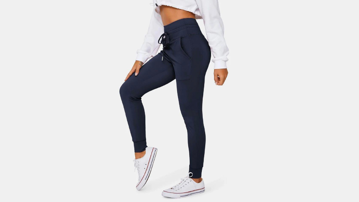 A model wearing navy joggers with a drawstring waist, paired with white sneakers and a white cropped sweatshirt against a light gray background.