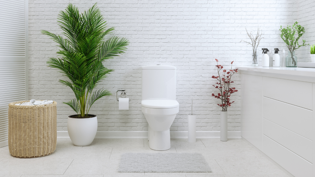 Bright and modern bathroom featuring a white toilet, potted plants, a wicker basket, and clean minimalist decor against a white brick wall.