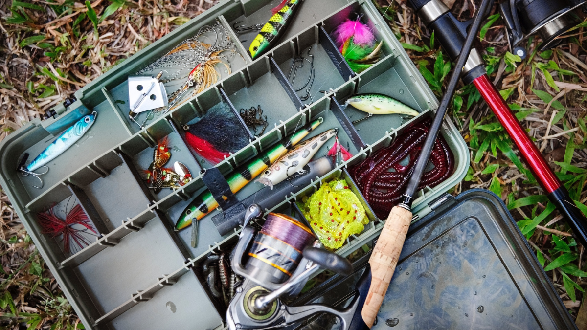 A fishing tackle box filled with lures, hooks, and bait, alongside a spinning reel and fishing rod. Ideal for anglers preparing for a fishing trip.