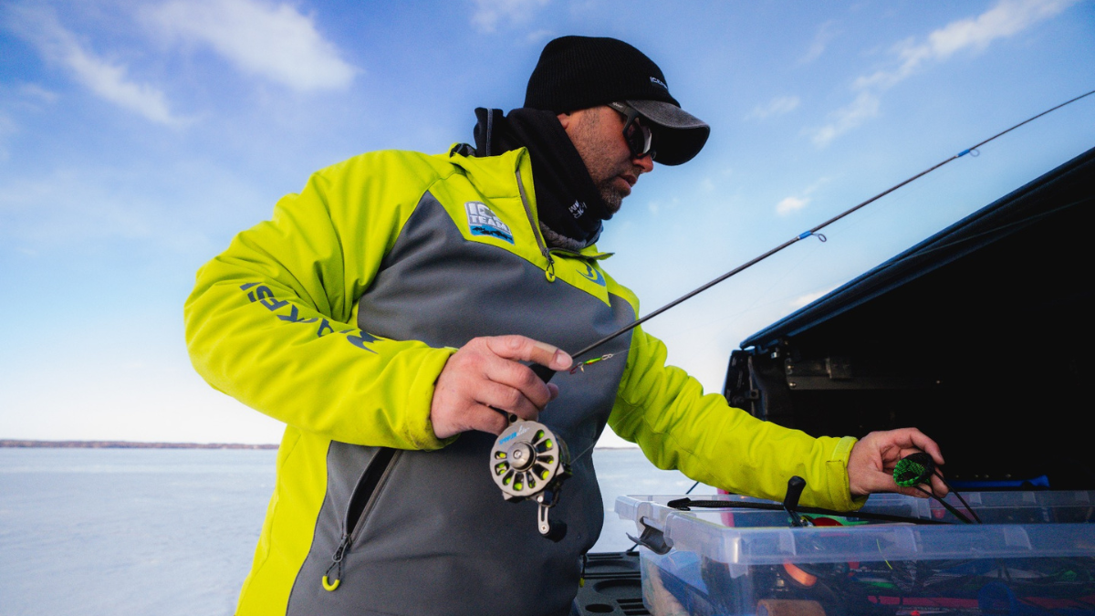 An ice fisherman dressed in cold-weather gear, preparing his fishing rod near a frozen lake.