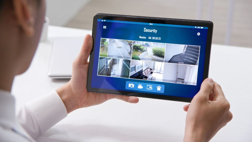 A person is holding a tablet displaying a live feed from multiple security cameras.