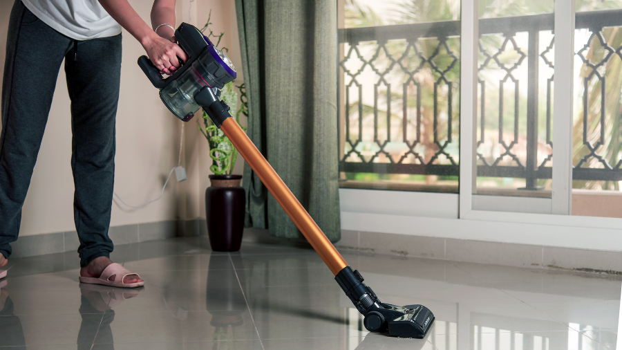 Person using a cordless vacuum cleaner on a tiled floor in a bright living space.